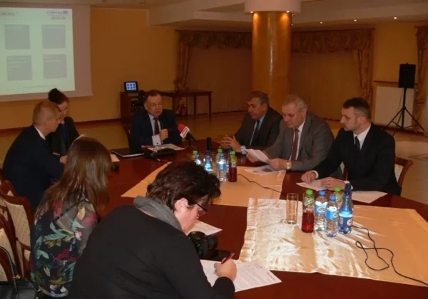 Grupa osób w garniturach prowadzi konferencję dotyczącą międzynarodowego projektu RUMOBIL w sali powiatu płockiego, przy stole z mikrofonami, dokumentami i butelkami wody.