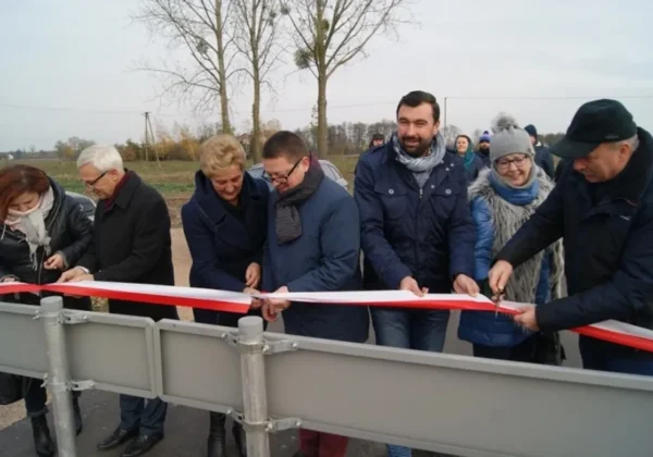 Grupa ludzi przecina czerwono-białą wstęgę na nowo wyremontowanym odcinku drogi w gminie Mała Wieś podczas uroczystego otwarcia.