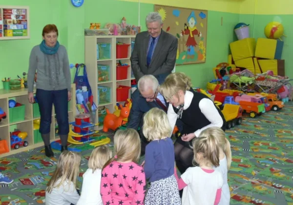 Grupa dorosłych rozmawia z słubickimi przedszkolakami w kolorowej sali zabaw pełnej zabawek.