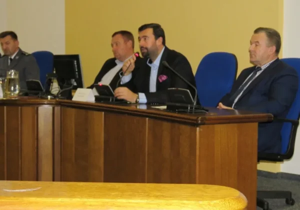Panel dyskusyjny podczas Ewaluacyjnej Debaty Społecznej: mężczyźni w garniturach siedzą za stołem, a jeden z nich przemawia do mikrofonu.