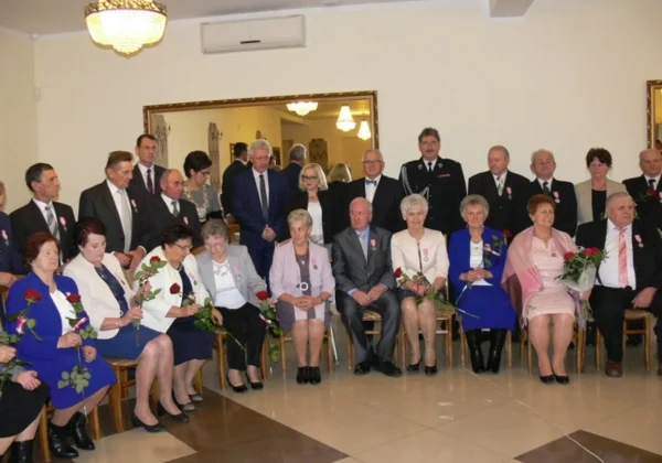 Grupa małżeństw z gminy Słubice podczas uroczystości wręczania medali i gratulacji, część siedzi z kwiatami, inni stoją w tle.