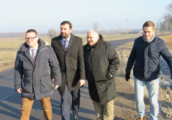 Czterech mężczyzn w zimowych kurtkach spaceruje po nowo wyremontowanym odcinku drogi powiatowej w Powiecie Płockim, na tle pól.