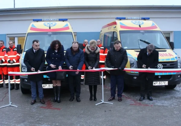 Uczestnicy uroczystości przecinają czerwoną wstęgę przed dwoma nowymi ambulansami stojącymi na placu przed siedzibą pogotowia w Płocku.