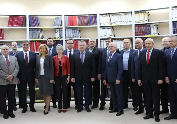 Grupa urzędników i radnych w garniturach stoi razem w biblioteczce technicznej przed regałami z teczkami; wśród nich znajdują się starosta i przewodniczący Rady przy Politechnice.
