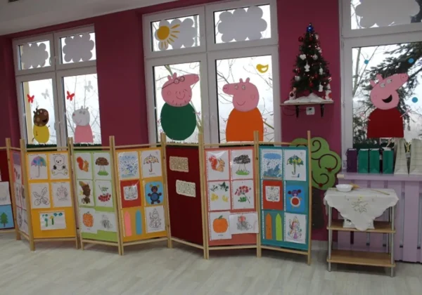 Wnętrze otwartej nowej części Żłobka Samorządowego w Gąbinie – kolorowe ścianki wystawowe z pracami dzieci, dekoracyjne postacie z bajki Świnka Peppa na oknach i świąteczna choinka.