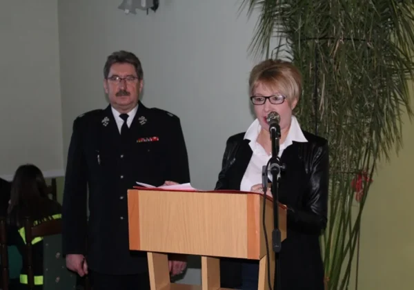 Kobieta w czarnej marynarce i białej koszuli przemawia do mikrofonu ze stojącego podium podczas VIII edycji konkursu ekologicznego dla OSP i MDP z powiatu płockiego; obok niej stoi mężczyzna w mundurze.