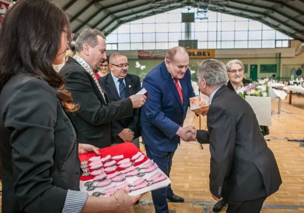 Grupa osób w eleganckich strojach wręcza medale i gratuluje małżeństwom z gminy Łąck podczas uroczystości w dużej hali.