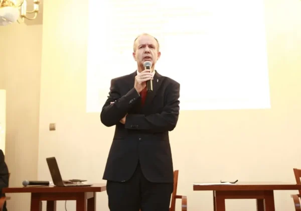Mężczyzna w czarnym garniturze przemawia do mikrofonu podczas prezentacji w sali konferencyjnej, na tle ekranu projekcyjnego w kontekście Płockiego Programu Onkologicznego.