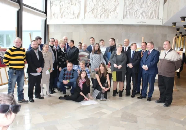 Grupa ludzi stojących i siedzących w holu parlamentu podczas wystawy Świat Sztuki znad Jaru.