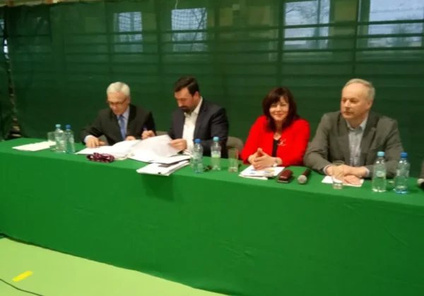 Czterech liderów samorządowych siedzi za zielonym stołem podczas spotkania w Małej Wsi, omawiając temat dróg; na stole leżą dokumenty, notatniki i butelki wody.
