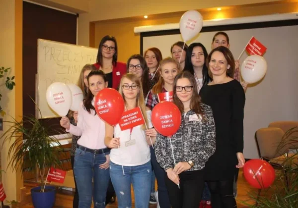 Grupa uczniów wraz z nauczycielką ze Zespołu Szkół w Wyszogrodzie podczas szkolnej akcji promującej oddawanie szpiku, trzyma balony i kartki z hasłem „Zostań dawcą szpiku”.