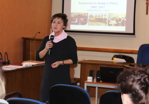 Kobieta trzyma mikrofon i prowadzi prezentację w sali konferencyjnej, na tle ekranu z slajtem o Partnerstwie Lokalnym w Polsce (2002–2017).