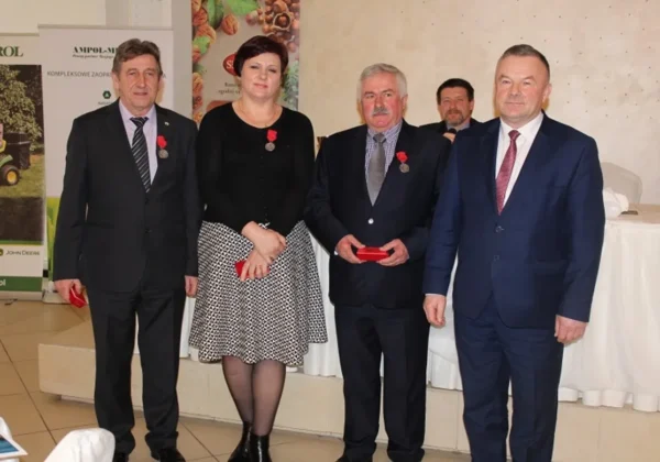 Czterech wyróżnionych hodowców bydła mlecznego stoi na scenie podczas ceremonii, ubranych w garnitury i elegancką sukienkę, z medalami na klatce piersiowej.