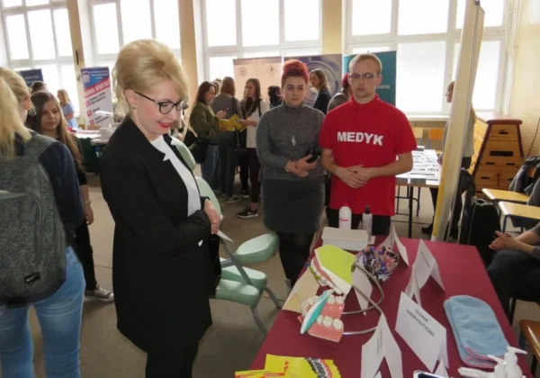 Uczestnicy VII Szkolnych Targ Edukacji i Pracy w Zespole Szkół im. St. Staszica w Gąbinie stoją przy stoisku z modelami dentystycznymi i materiałami edukacyjnymi.