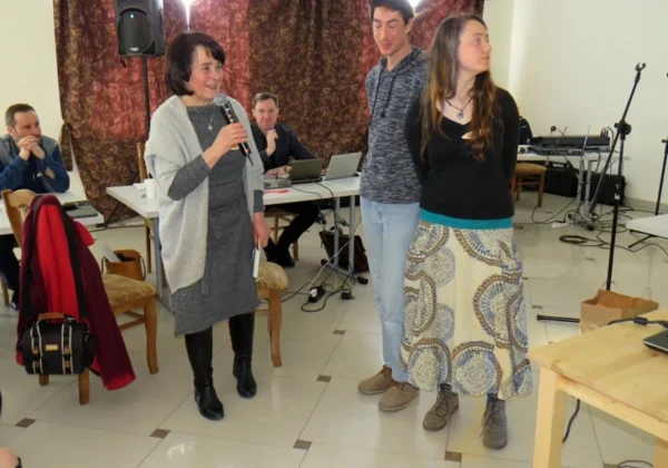 Kobieta trzyma mikrofon i przemawia podczas seminarium Dobre Żniwa, stojąc obok dwóch uczestników, w sali z laptopami i sprzętem nagłaśniającym.