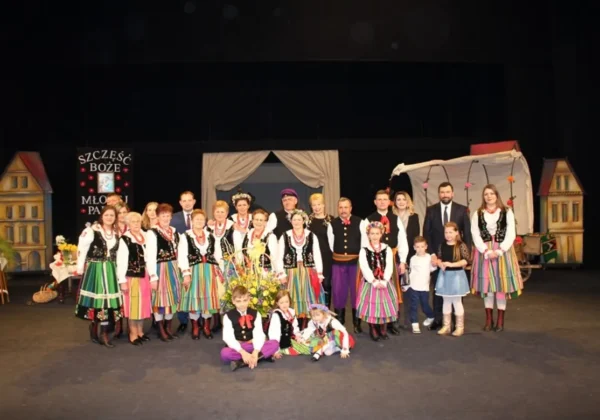 Grupa osób w kolorowych, tradycyjnych strojach ludowych stoi na scenie Teatru Dramatycznego w Płocku z okazji Dnia Kobiet.