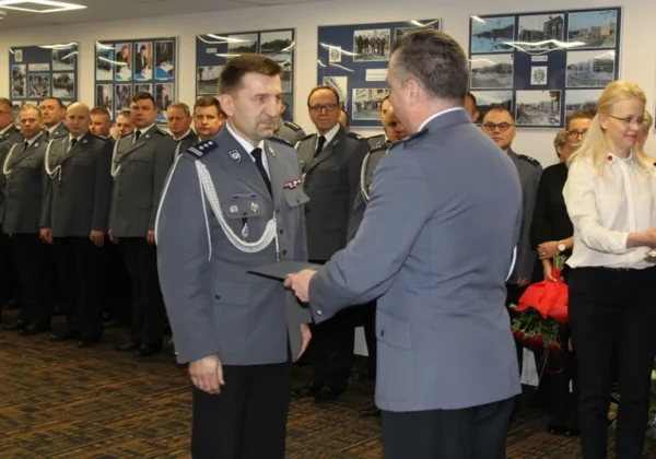 Uroczystość pożegnania Komendanta Miejskiego Policji w Płocku: oficer wręcza dokument innemu oficerowi, a w tle stoi linia policjantów w mundurach.