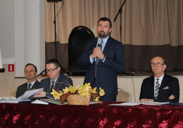 Mężczyzna w granatowym garniturze przemawia do zebranych przy stole podczas spotkania liderów miasta i gminy Gąbin.