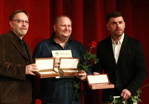 Trzech mężczyzn na scenie przed czerwonymi zasłonami trzyma nagrody w drewnianych pudełkach oraz różę, podczas Dnia Teatru i Srebrnych Masek.