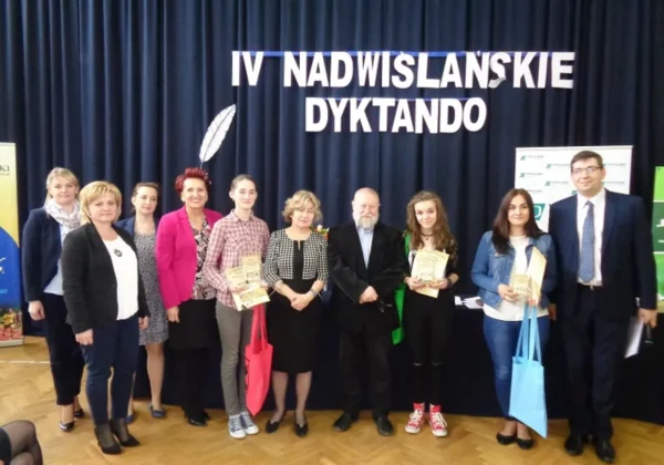 Grupa osób stoi na scenie podczas IV Nadwiślańskiego Dyktanda, część z nich trzyma certyfikaty i torby, a w tle wisi czarna kurtyna z napisem.