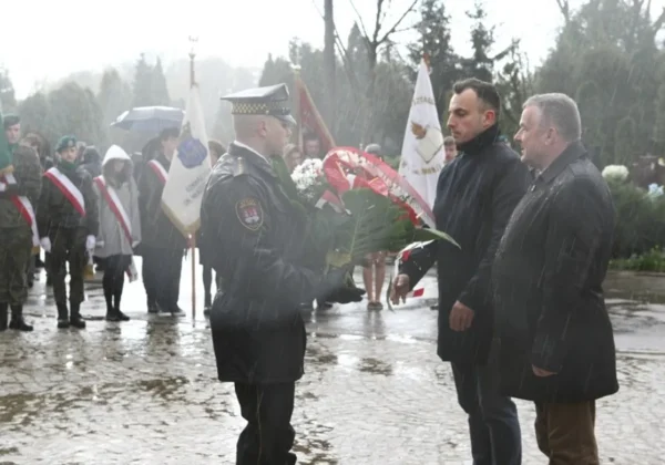 Funkcjonariusz składa wieniec podczas uroczystości odsłonięcia Memoriału Sybiraków i Płocczan Pomordowanych na Wschodzie, w deszczowy dzień.
