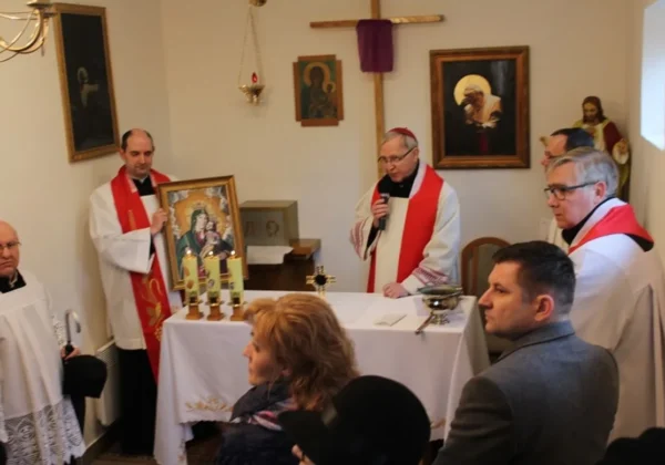 Kameralne nabożeństwo w kaplicy DPS w Goślicach przy ołtarzu z relikwiami św. Jana Pawła II i ikoną Matki Bożej, prowadzone przez duchowieństwo w białych albach z czerwonymi dodatkami.