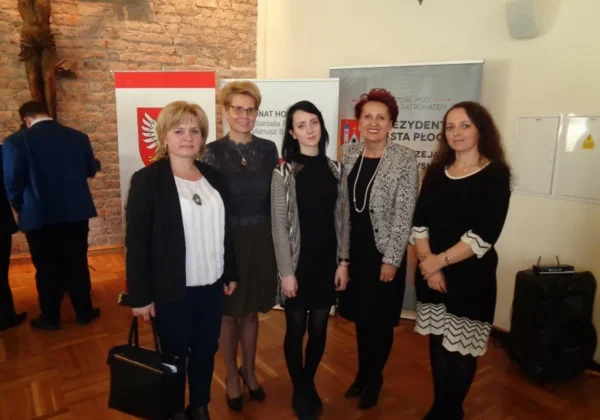 Pięć kobiet stoi razem na tle banerów z herbem Polski, w eleganckich ubraniach, podczas wydarzenia „O Szablę Komendanta”.