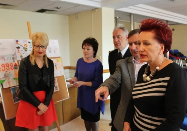 Grupa osób podczas rozstrzygnięcia Konkursu Plastycznego „25 lat PSP – Profesjonalni, Sprawni, Pomocni”, stojąca obok tablicy z nadesłanymi pracami.