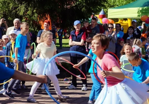 Grupa dzieci i dorosłych podczas plenerowego XI Letniego Pikniku Integracyjnego w Zespole Szkół Specjalnych w Goślicach, kręcą kolorowymi hula-hop.