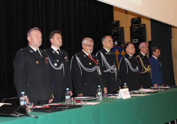 Grupa strażaków w czarnych mundurach z odznaczeniami stoi na scenie podczas IV Zjazdu Oddziału Wojewódzkiego ZOSP RP.