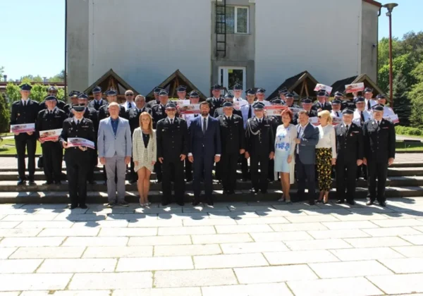 Grupa strażaków OSP z powiatu płockiego w mundurach oraz goście w garniturach stoją na schodach przed budynkiem podczas uroczystej ceremonii wręczania nagród.