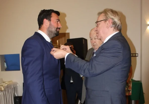 Dwóch mężczyzn w garniturach, jeden przypina drugiemu odznakę podczas jubileuszu 70-lecia Spółdzielni Rzemieślniczej „Wielobranżowa”.
