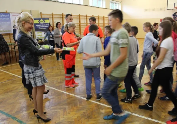 Dzieci stoją w hali sportowej w Nowym Duninowie, a pracownicy kampanii Jesteś widoczny, jesteś bezpieczny wręczają im materiały promocyjne.