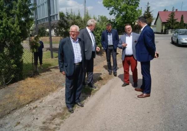 Grupa pięciu mężczyzn w garniturach stoi na poboczu drogi podczas wizyty roboczej przy przebudowie drogi powiatowej nr 1454W (Sanniki – Grabowiec – Słubice).