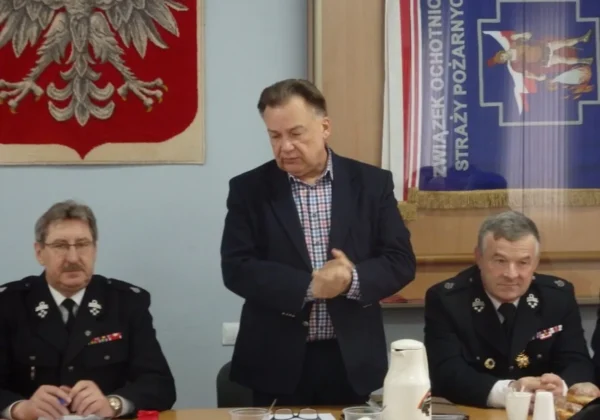 Trzech mężczyzn przy stole podczas pierwszego posiedzenia Zarządu Oddziału Powiatowego ZOSP RP w Płocku w kadencji 2016–2021; pośrodku stoi mężczyzna w garniturze, a po bokach siedzą strażacy w mundurach.