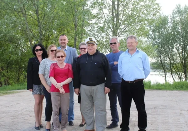 Grupa osób stoi razem na świeżym powietrzu, na tle drzew i jeziora, podczas posiedzenia Powiatowej Rady ds. Osób Niepełnosprawnych.