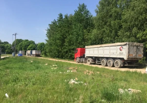 Długi konwój ciężarówek jedzie drogą przez zielone, zalesione tereny; rozpoczęto wywóz odpadów z Ciółkowa.