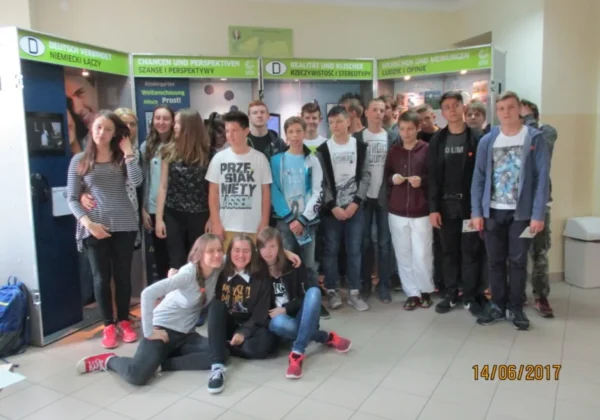 Grupa uczniów stoi i siedzi w holu szkoły przed stanowiskami wystawy multimedialnej Deutschland im Koffer – Niemcy w walizce w Zespole Szkół im. Stanisława Staszica w Gąbinie.
