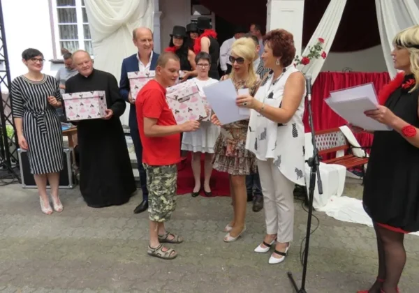 Grupa osób na zewnątrz sceny wręcza upominki i dokumenty podczas uroczystości z okazji 70-lecia DPS w Koszelewie.