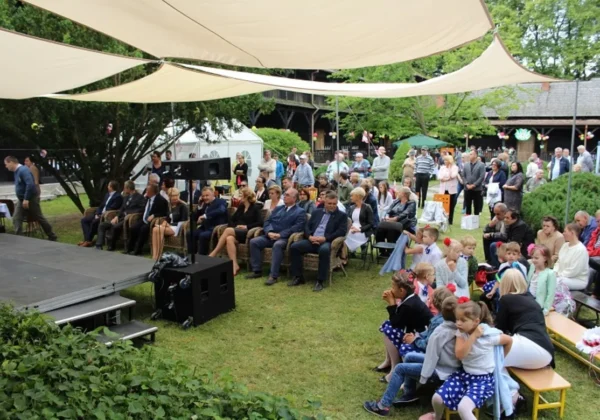 Uczestnicy plenerowej imprezy z okazji imienin Antoniego w Domu Pomocy Społecznej w Brwilnie, siedzący przy scenie w ogrodzie pod dużymi parasolami.