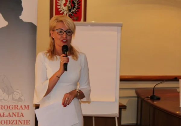 Kobieta w białej sukni z mikrofonem przemawia podczas konferencji antyprzemocowej.