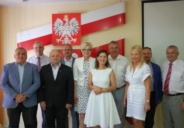 Grupa urzędników samorządowych stoi razem na sali konferencyjnej, na tle polskiej flagi i godła podczas Spotkania Starostów.