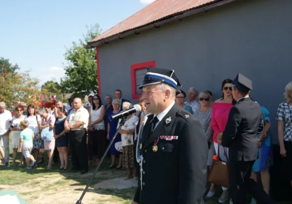 Uroczystość 70-lecia OSP w Nowych Karwosiekach: mężczyzna w strażackim mundurze z odznaczeniami przemawia do mikrofonu przed zgromadzonymi mieszkańcami i gośćmi podczas nadania sztandaru.