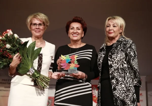 Trzy kobiety stoją na scenie podczas jubileuszu Książnicy; po lewej trzyma bukiet róż, w środku prezentuje kolorową statuetkę składającą się z elementów, a po prawej stoi w wzorzystym płaszczu.