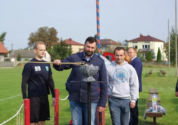 Trzech mężczyzn stoi na boisku podczas ceremonii III Mazowieckiego Turnieju Piłki Nożnej o Puchar Starosty Płockiego „W Dolinie Rzeki Wisła”, obok wysokiego pucharu ustawionego na stojaku.