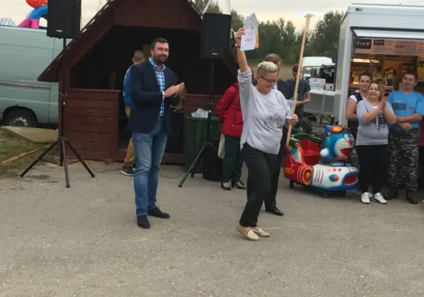 Uczestniczka Turnieju Sołectw Gminy i Miasta Wyszogród w Rakowie dumnie unosi dyplom nad głową, a zgromadzeni wokół organizatorzy i widzowie ją oklaskują.