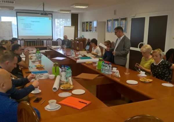 Uczestnicy szkolenia kadry obrony cywilnej powiatu płockiego siedzą przy długim stole w sali konferencyjnej, słuchając prezentacji wyświetlanej na projektorze, z notatkami, napojami i przekąskami na stole.