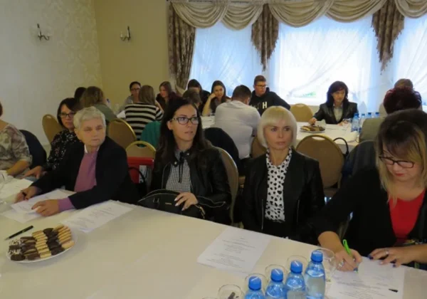 Grupa uczestników III Konferencji Partnerstwa Lokalnego powiatu płockiego siedzi przy stole w sali konferencyjnej, mając przed sobą dokumenty, notatniki, wodę i przekąski.