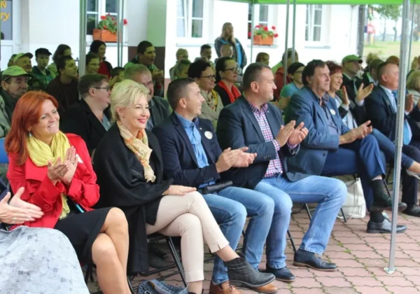 Grupa uczestników siedzi pod zielonym namiotem w Goślicach podczas Dnia pieczonego ziemniaka, klaskając.
