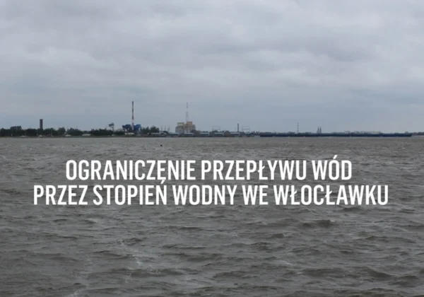 Widok na rzekę z zabudowaniami przemysłowymi na horyzoncie i duży napis informujący o ograniczeniu przepływu wód przez stopień wodny we Włocławku.